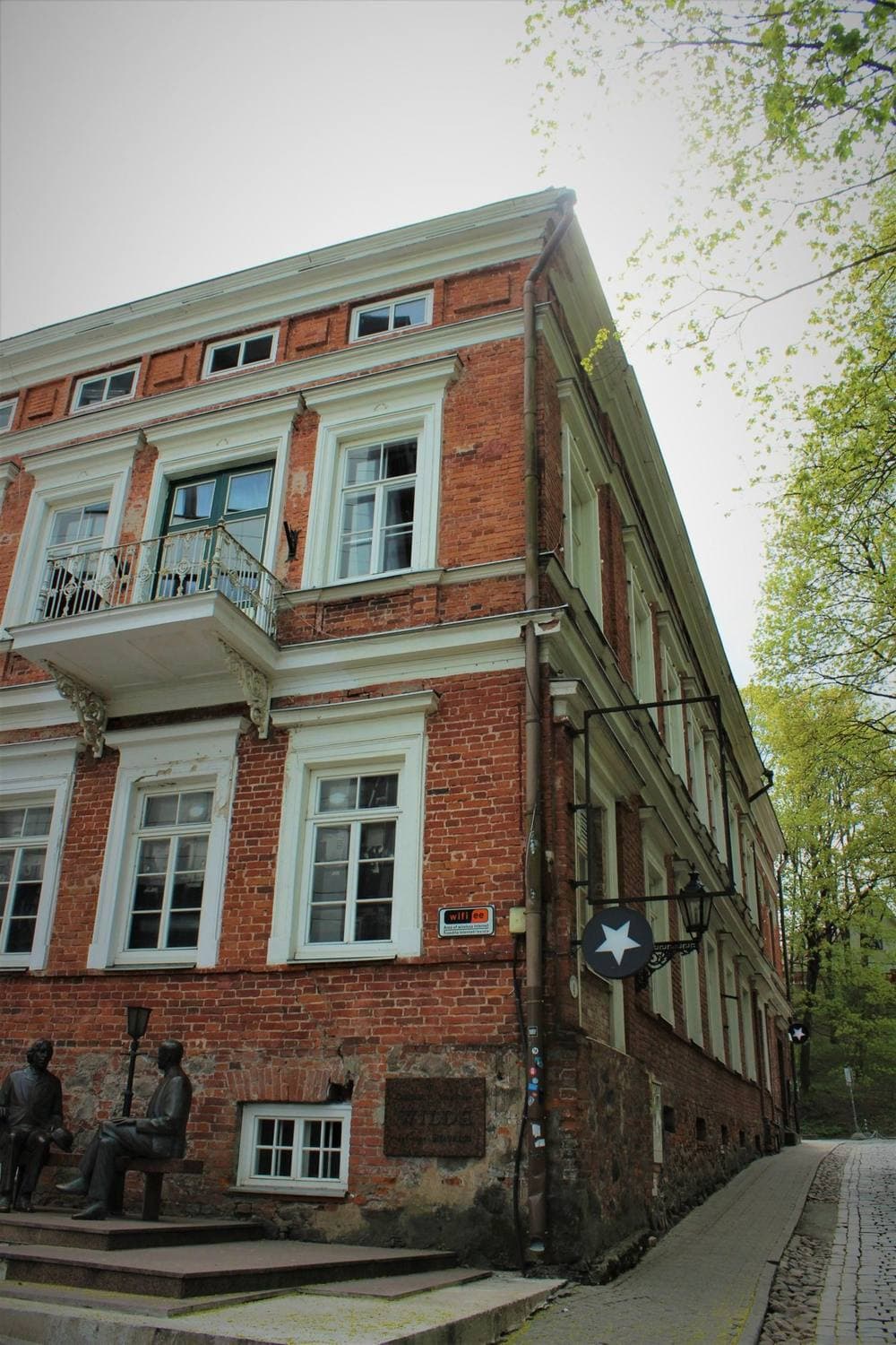 Vana telliskivist trükikoja hoone Vallikraavi tänaval, ukse ees pronksist Eduard Vilde ja Oscar Wilde